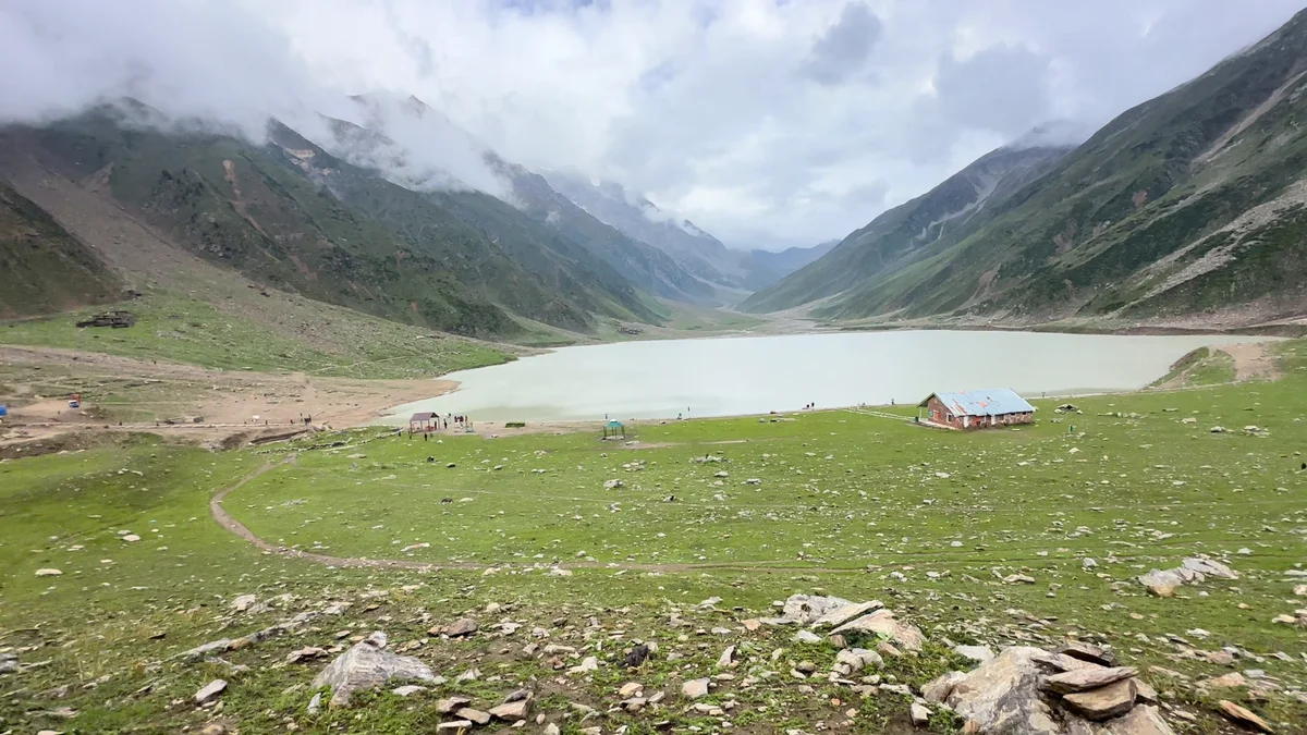 A pale mountain lake and green meadow beneath low clouds