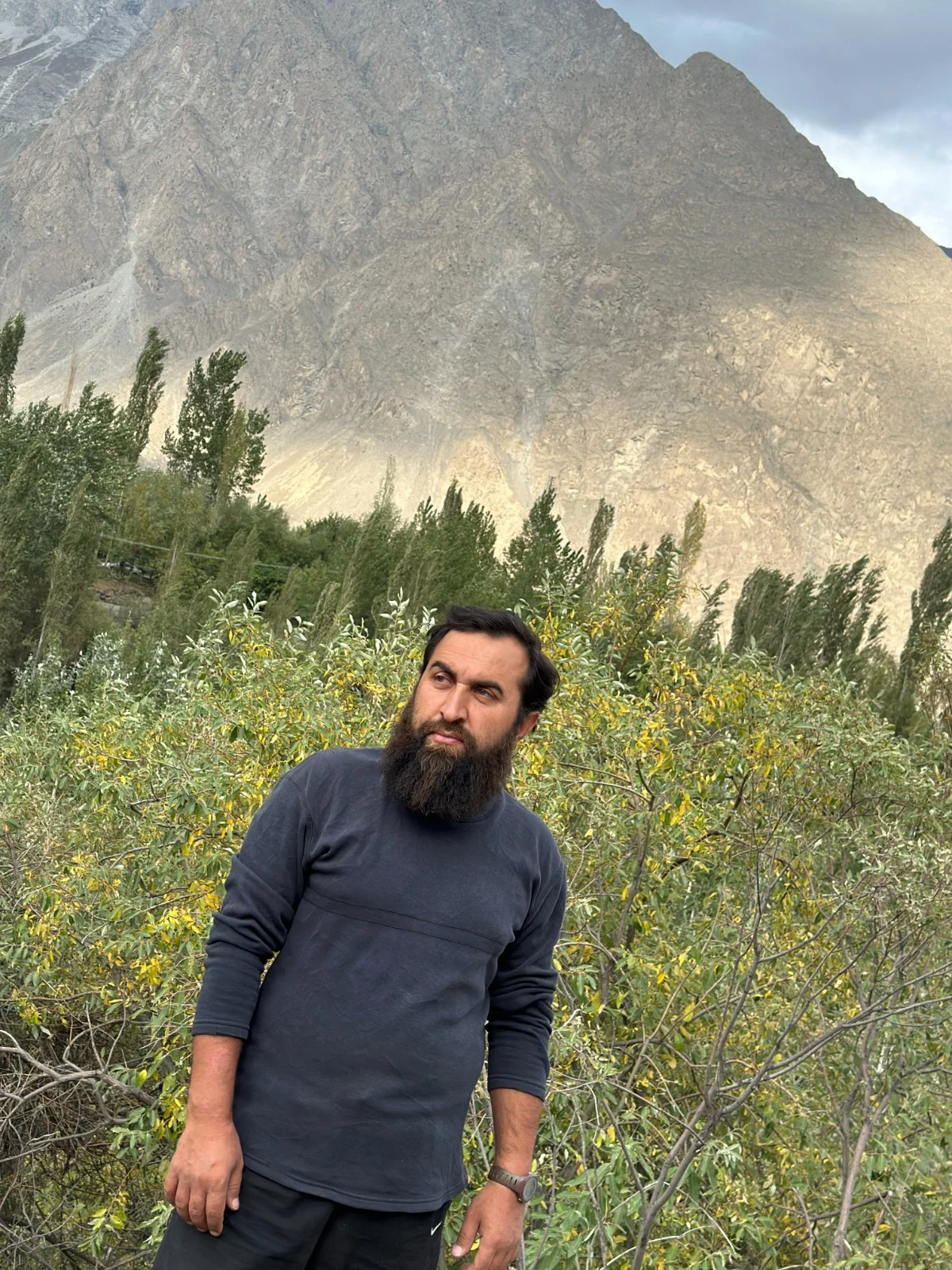 Abdullah among sunlit foliage below a mountain slope