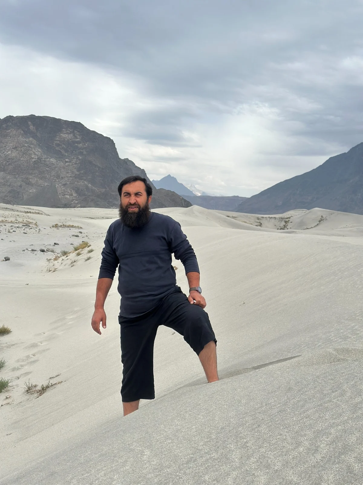 Abdullah walking across pale sand dunes between mountains