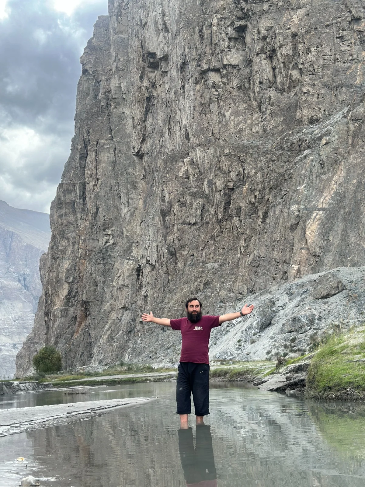 Abdullah standing in still water below a tall rock face with arms outstretched