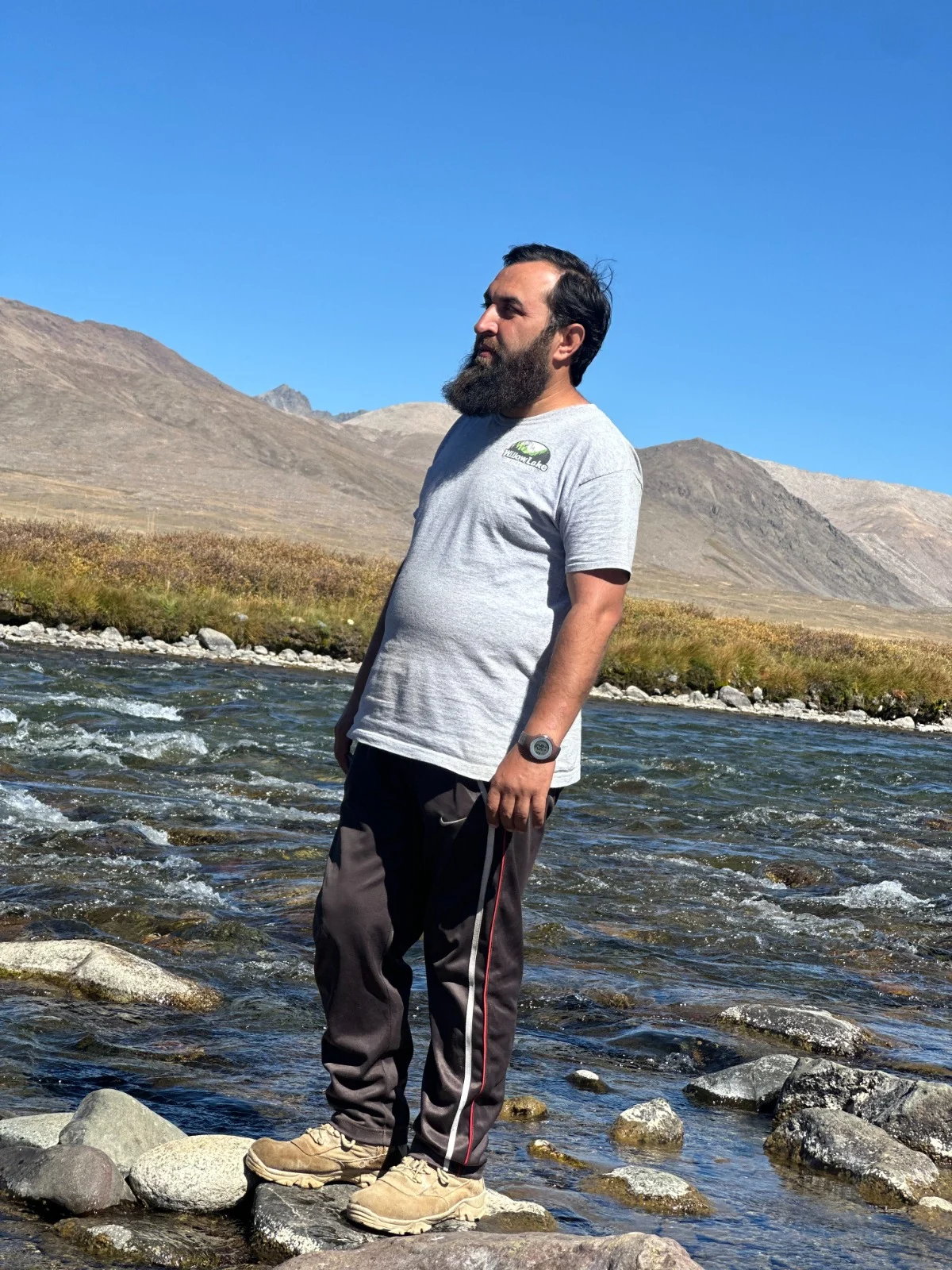 Abdullah on rounded stones beside a sunlit mountain stream