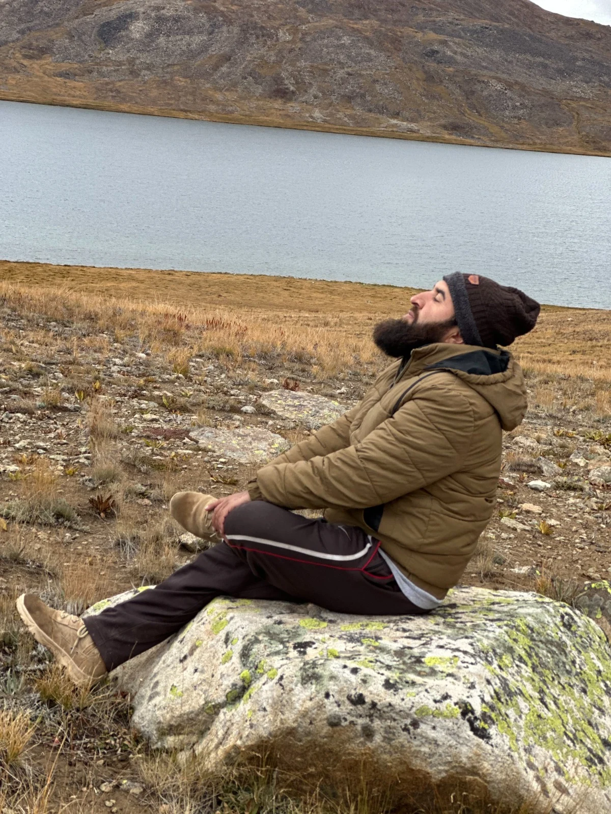 Abdullah resting on a rock beside a lake in an autumn mountain landscape